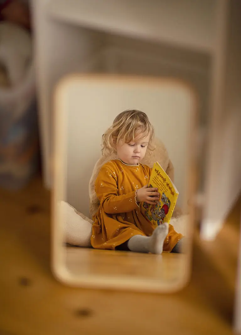 Petite fille tenant un livre devant un miroir, symbole de l’enfant intérieur et des blessures émotionnelles