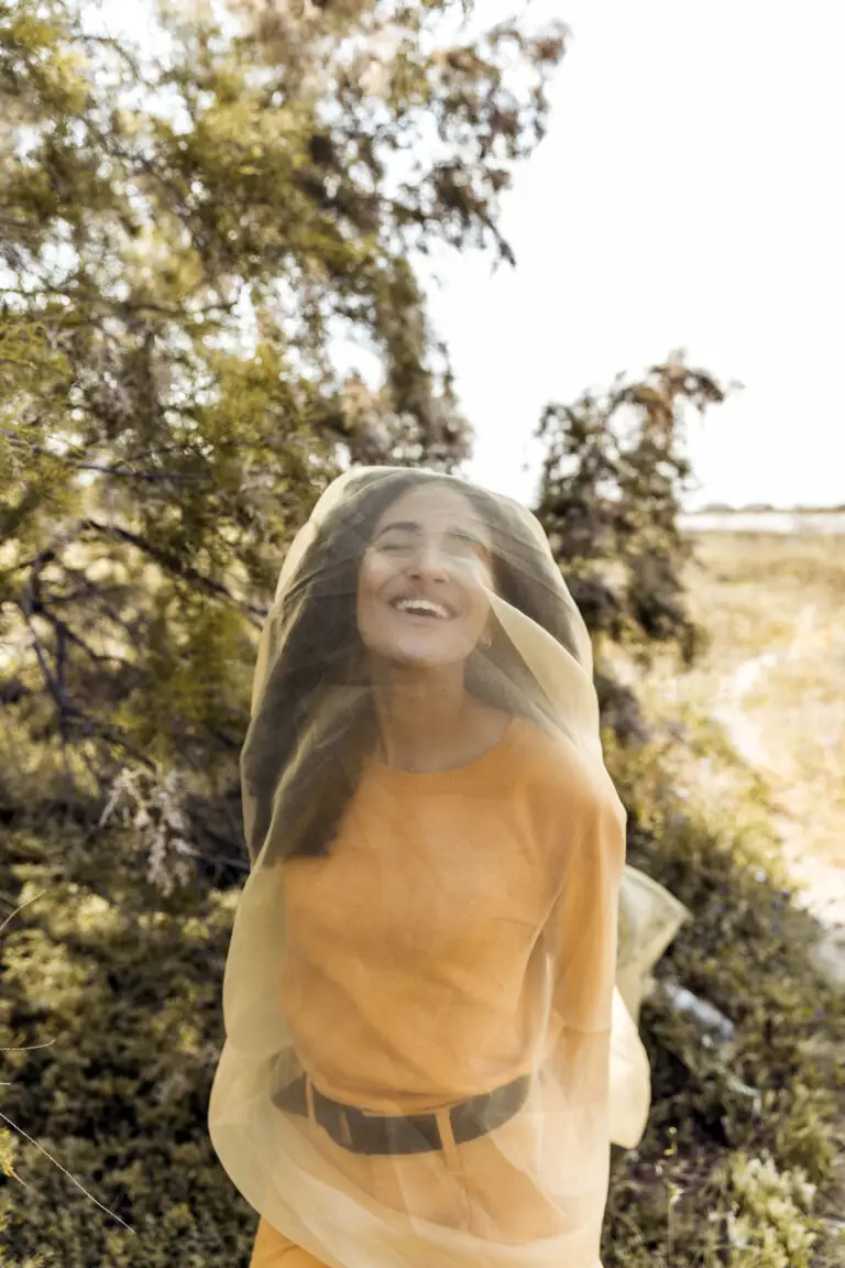 Jeune femme souriante dans la nature, enveloppée d’un voile léger