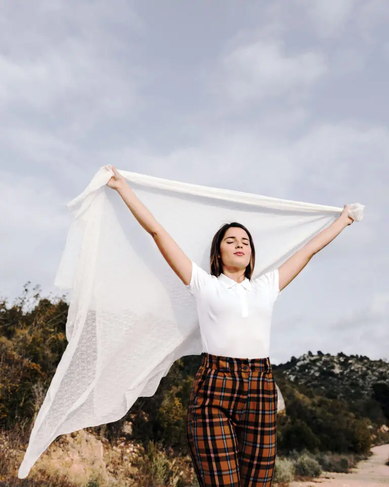 Jeune femme souriante dans la nature, qui tient un voile levé au-dessus de sa tête.