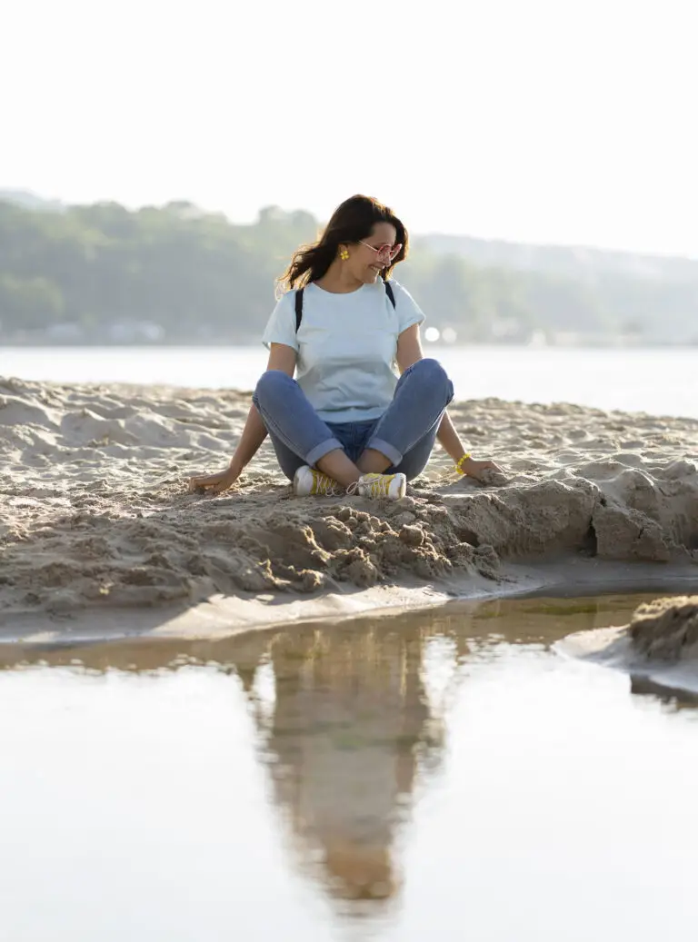 Jeune femme assise au bord d’un plan d’eau, observant son reflet brouillé dans l’eau