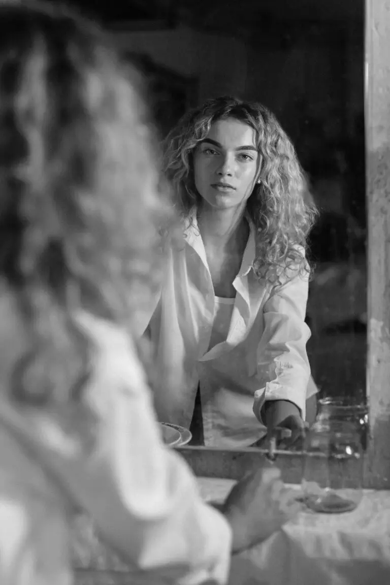 Jeune femme de dos face à un miroir dans une salle de bain, photographie en noir et blanc
