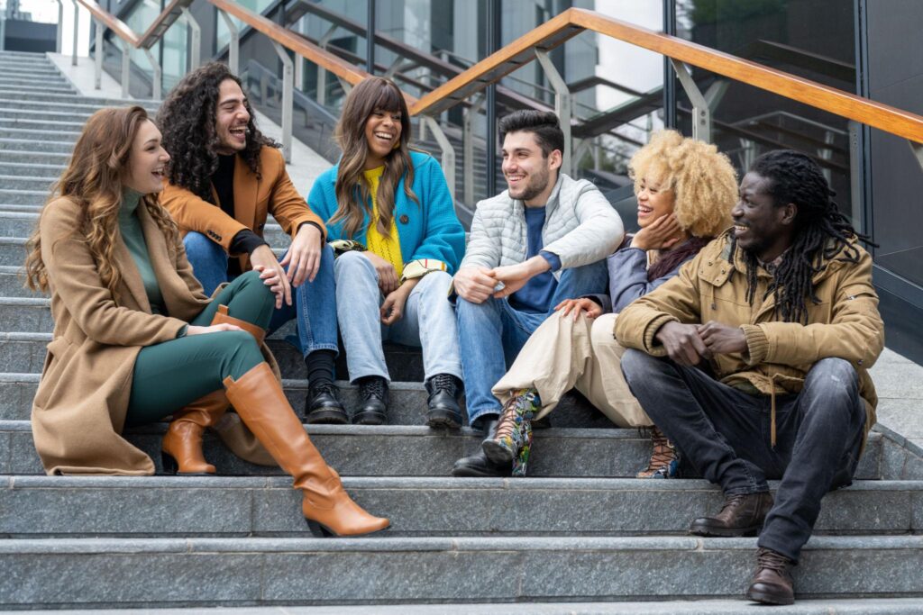 Jeunes adultes d’origines diverses réunis sur les marches d’un bâtiment, dans un moment de partage et de convivialité.