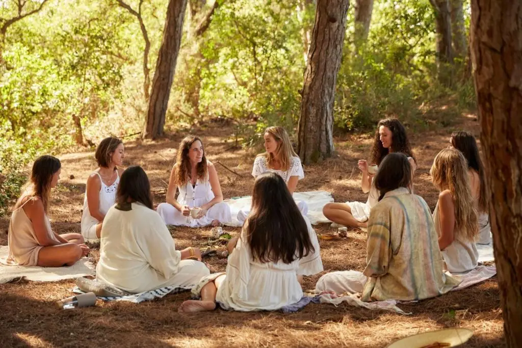 Cercle de femmes réunies en pleine nature, assises autour d'un tissu entouré de fleurs sauvages, symbole de sororité, d'écoute et de partage.