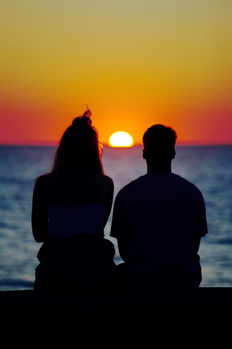 Un couple assis côte à côte regardant le soleil se coucher.